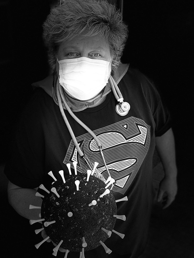Person wearing a superhero t-shirt and mask, holding a model of a virus with syringes in it.