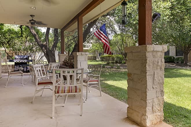 A cozy patio with outdoor seating and a view of the garden, featuring a flag and surrounded by trees.