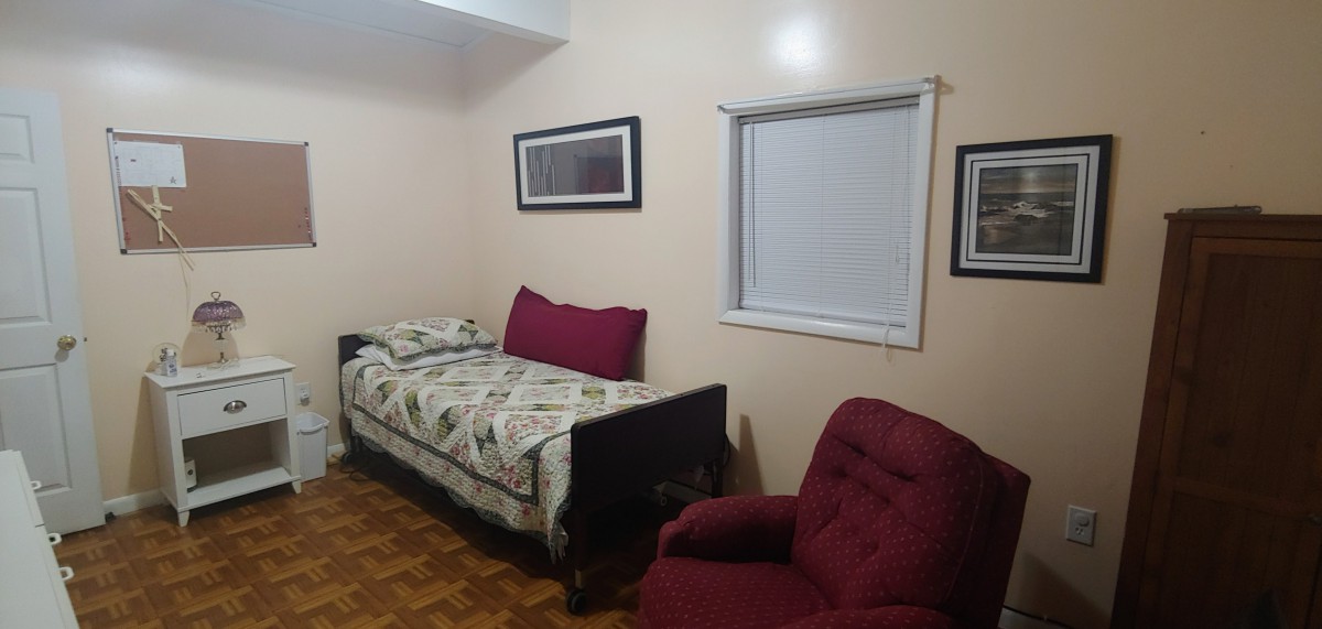A simple bedroom with a single bed, burgundy armchair, and framed pictures on the wall.