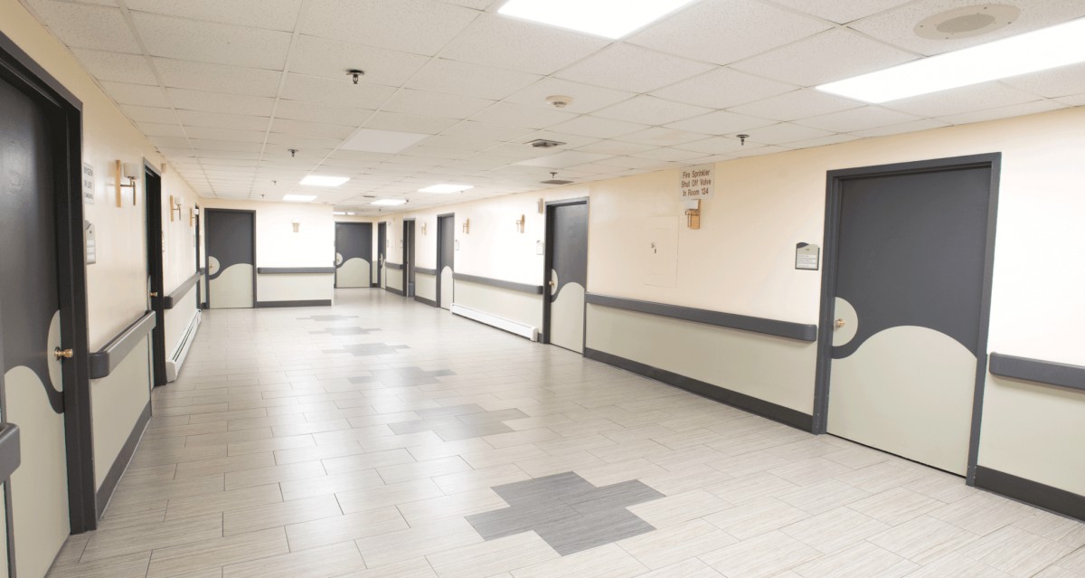 An empty hospital corridor with overhead lights and closed doors.