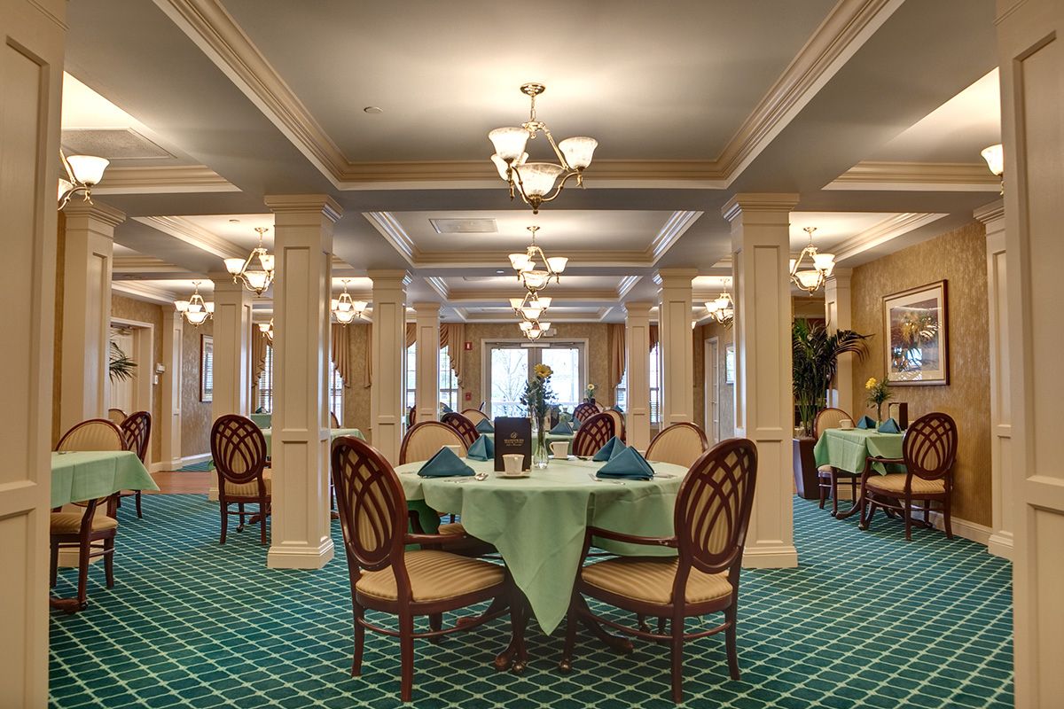 A spacious and elegantly decorated dining room with neatly arranged tables and chairs, illuminated by chandeliers.