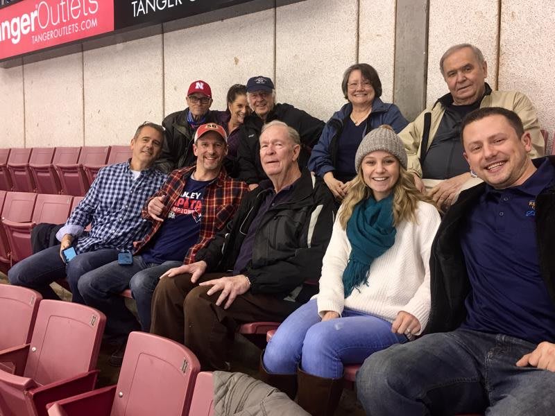 A group of people smiling while seated indoors, dressed in casual winter clothing.