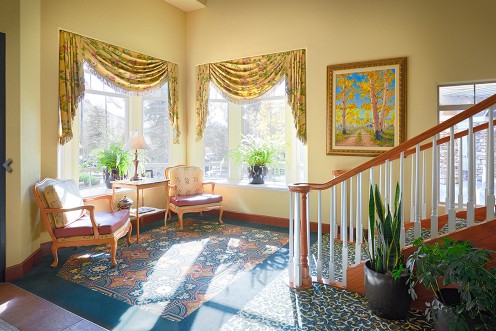 A well-lit living room with a staircase, featuring elegant furniture and lush green plants.