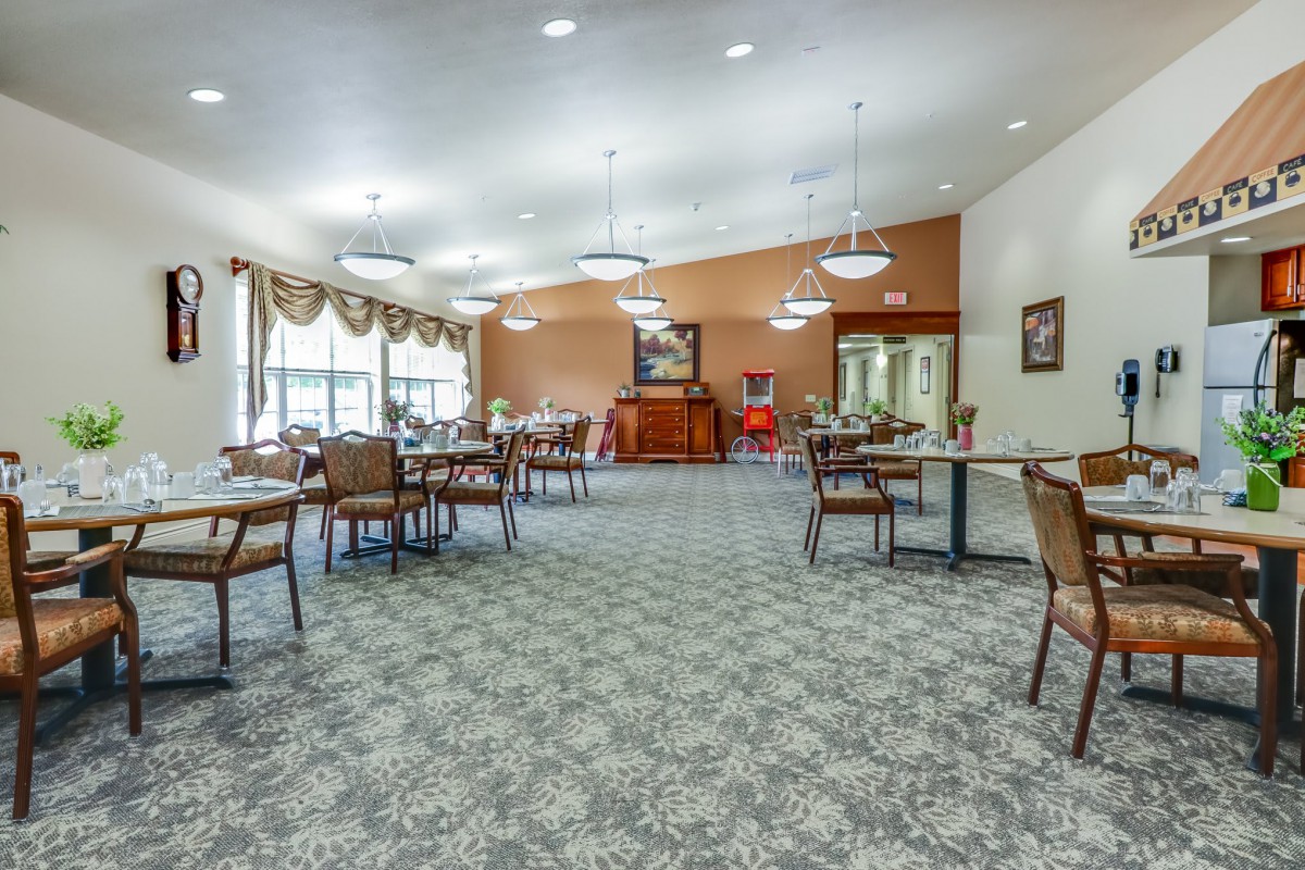 A spacious dining area with multiple tables and chairs, featuring elegant lighting and carpeted floors.