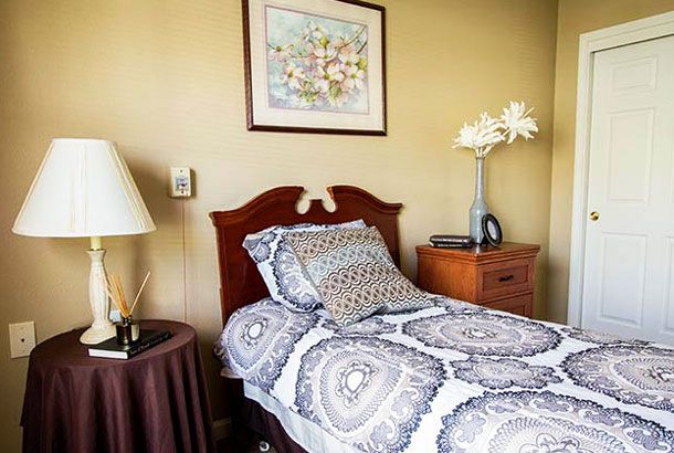 A cozy bedroom with a neatly made bed, a decorative pillow, and a nightstand adorned with a flower vase and lamp.