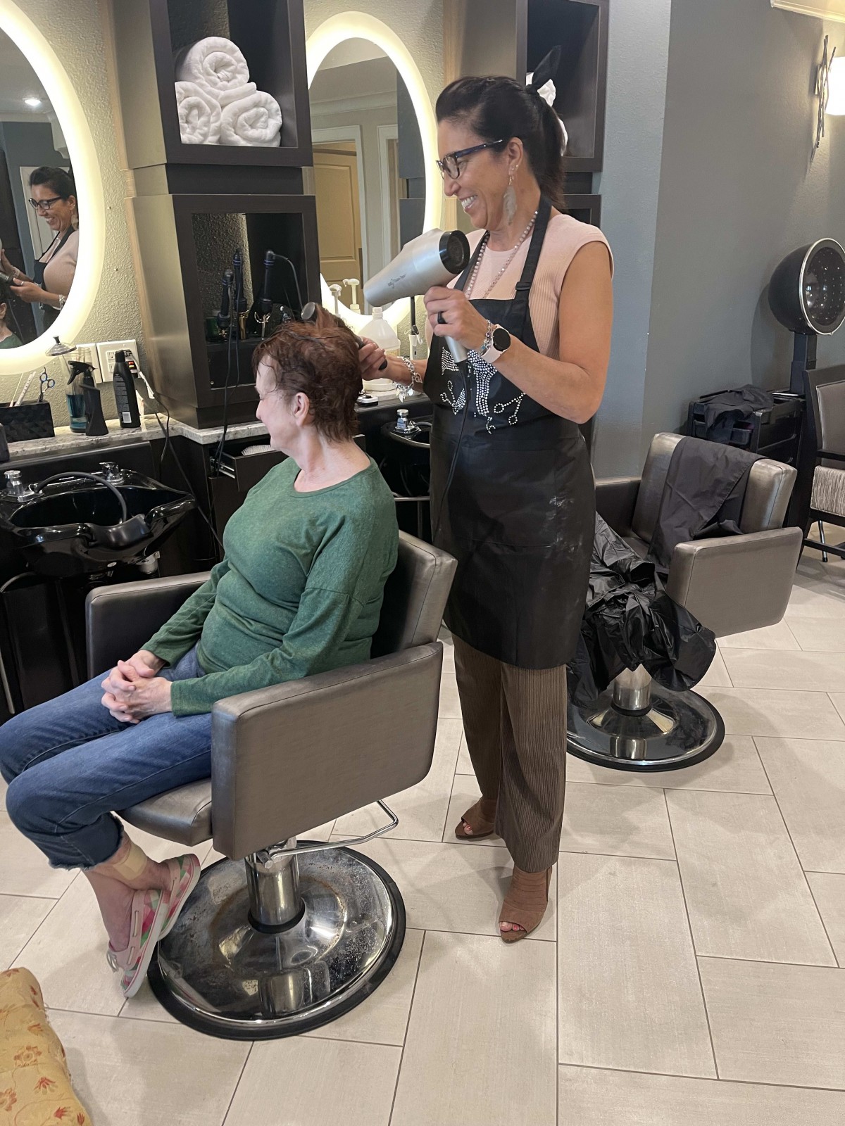 A hairstylist blow dries a client's hair in a salon.
