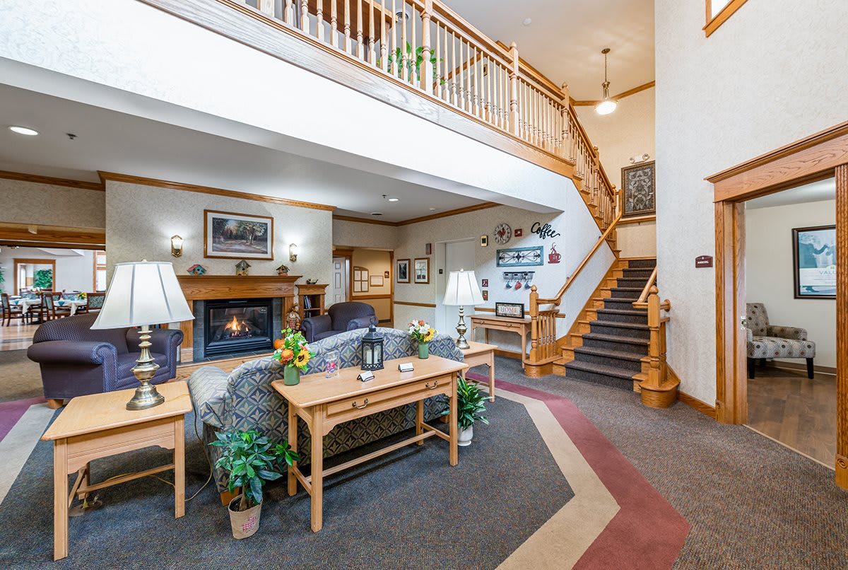 A cozy living room interior featuring a fireplace, comfortable seating, a staircase, and decorative elements.
