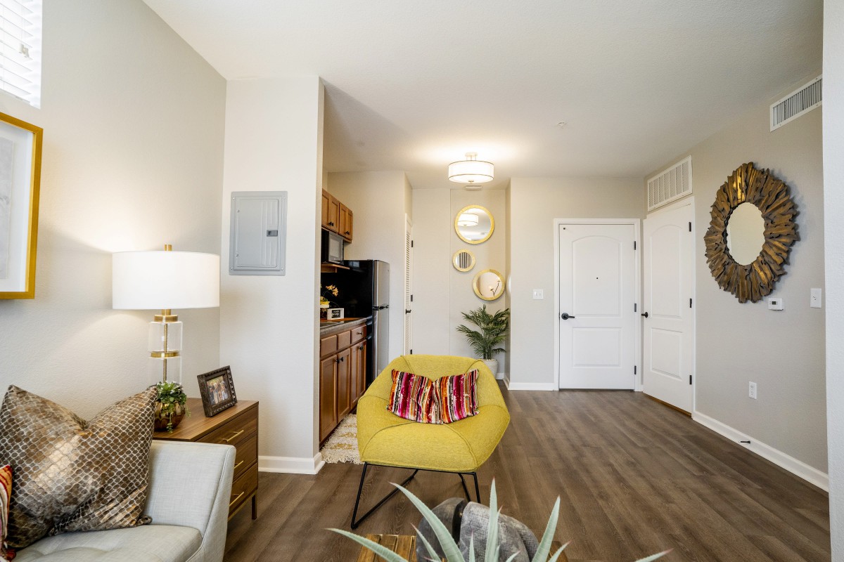 A modern living room with a yellow chair, wood flooring, and neutral decor.