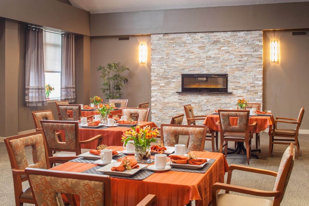 A warmly decorated dining room with tables set for a meal, featuring orange tablecloths and a modern fireplace.