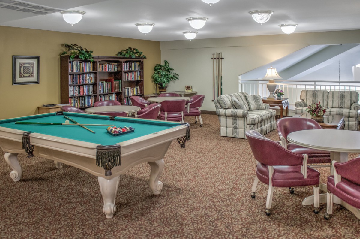 A cozy game room featuring a pool table and a small library with comfortable seating.