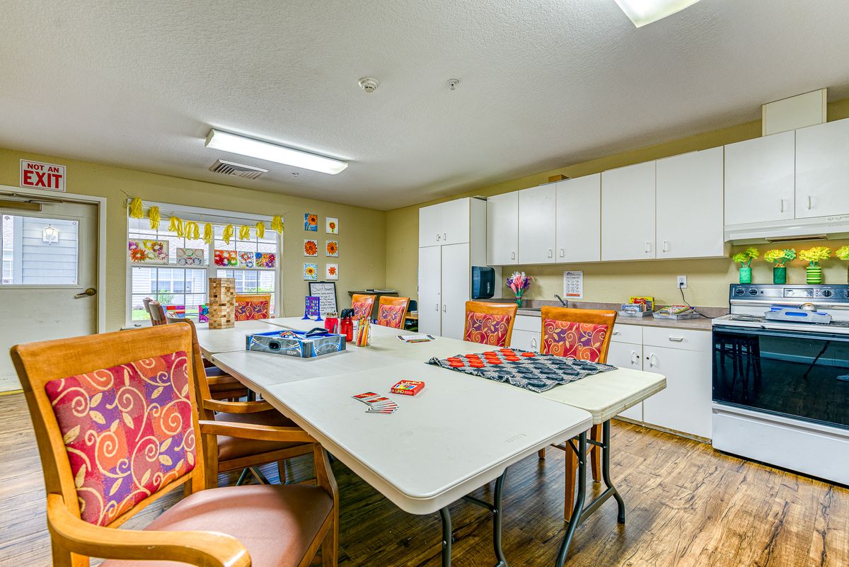 A brightly lit meeting room with a large table surrounded by chairs, adjacent to a kitchenette area.
