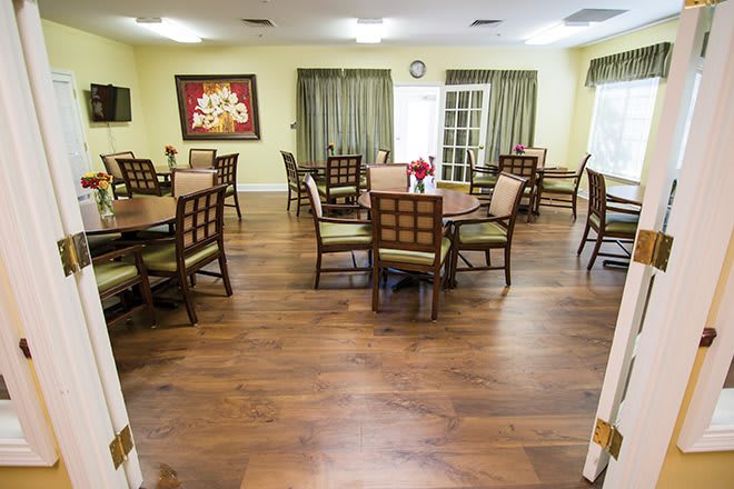 A spacious dining room with multiple tables and chairs, featuring wooden flooring and decorative artwork.