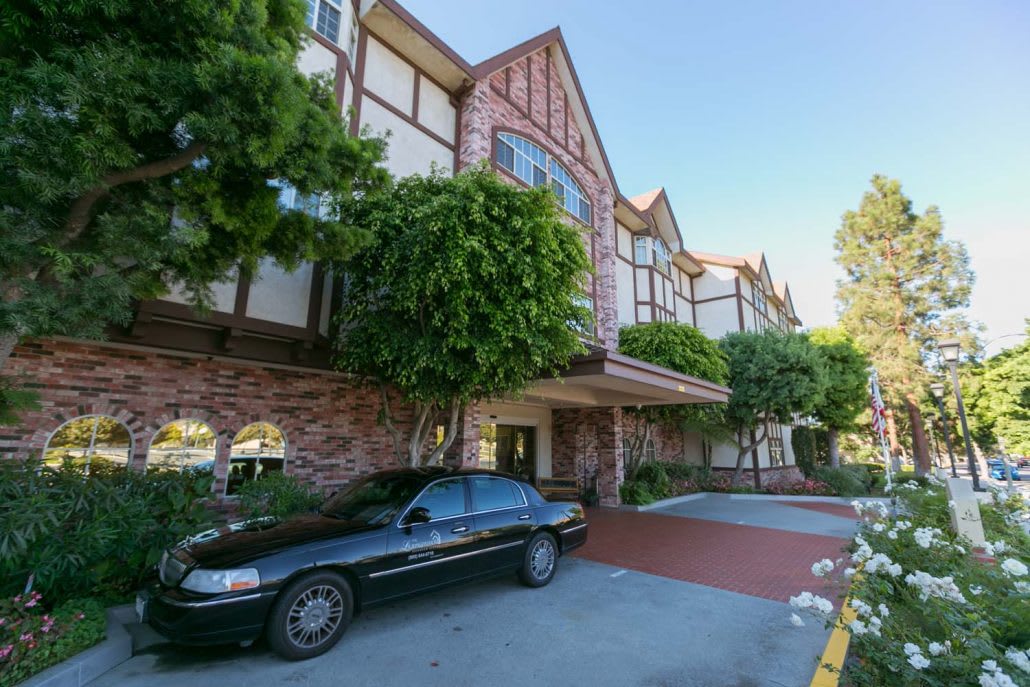 A residential building featuring Tudor-style architecture with a parked car in the driveway and trees lining the entrance.