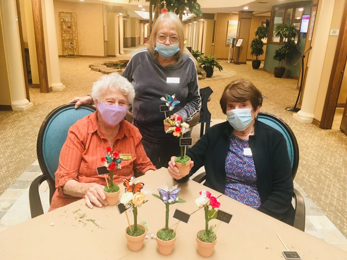 A group of seniors enjoying a crafting session indoors, creating colorful flower arrangements while wearing masks.