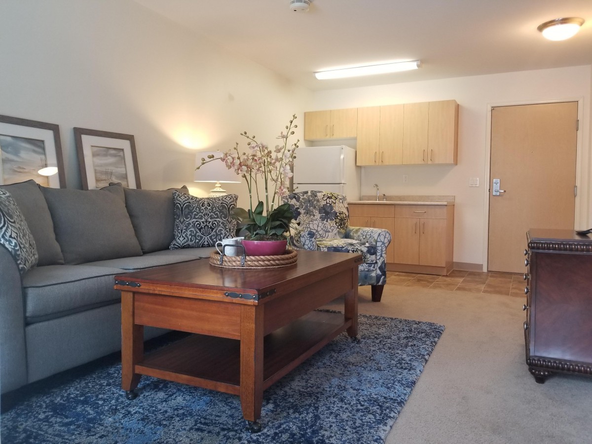 A cozy living room with a sofa, coffee table, and kitchenette in the background.