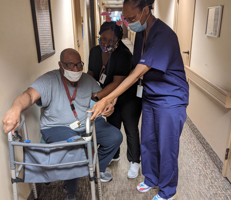 Healthcare professionals assisting a patient with a walker in a hospital corridor.