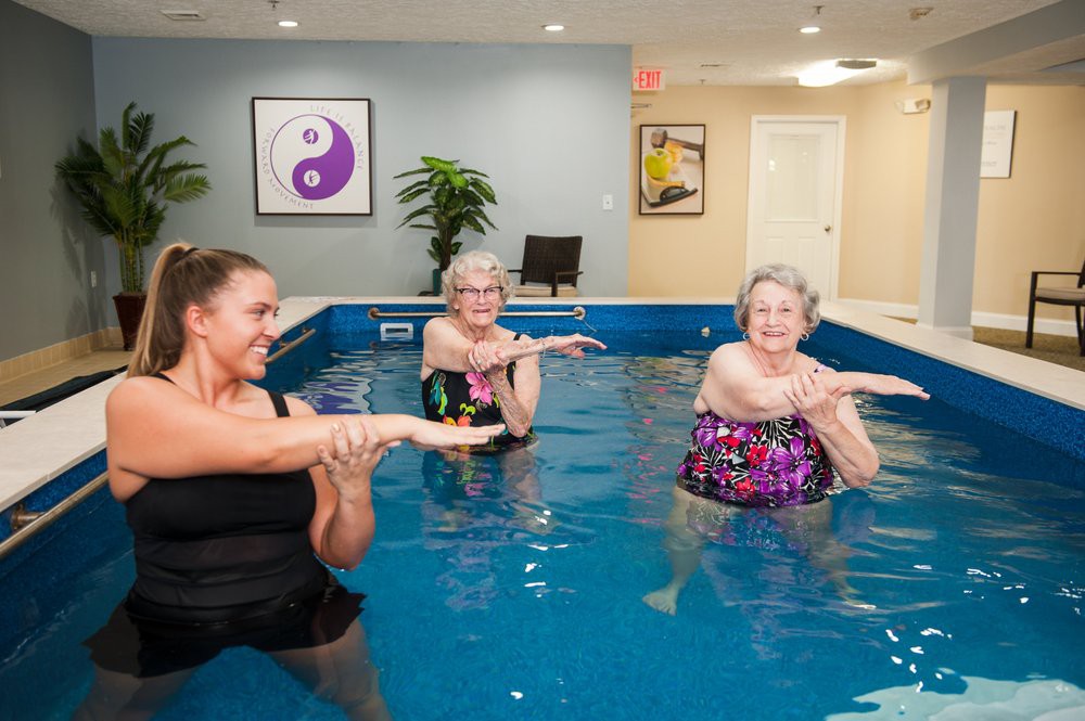 A group of elderly women engaging in water aerobics in an indoor swimming pool.
