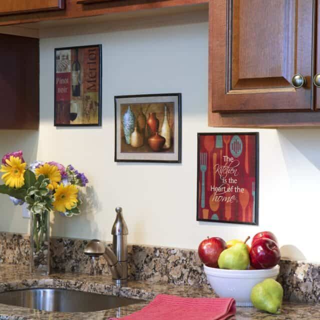 A cozy kitchen corner with wall art and a countertop displaying flowers and fruits.