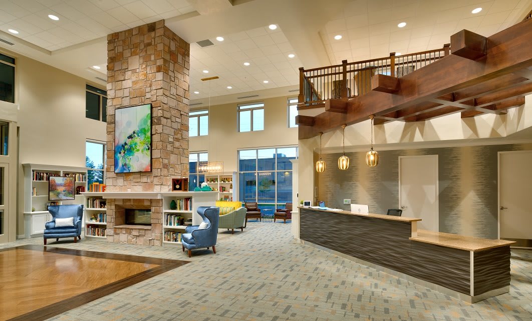 A modern lobby area featuring a stone fireplace, reception desk, and wooden staircase.