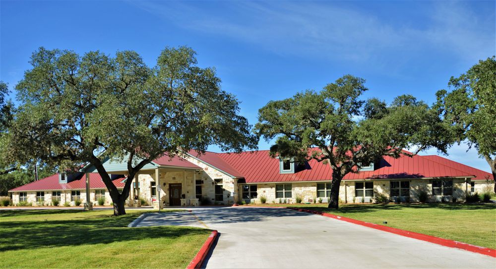 A residential building with a red roof, surrounded by trees and a driveway under a clear blue sky.