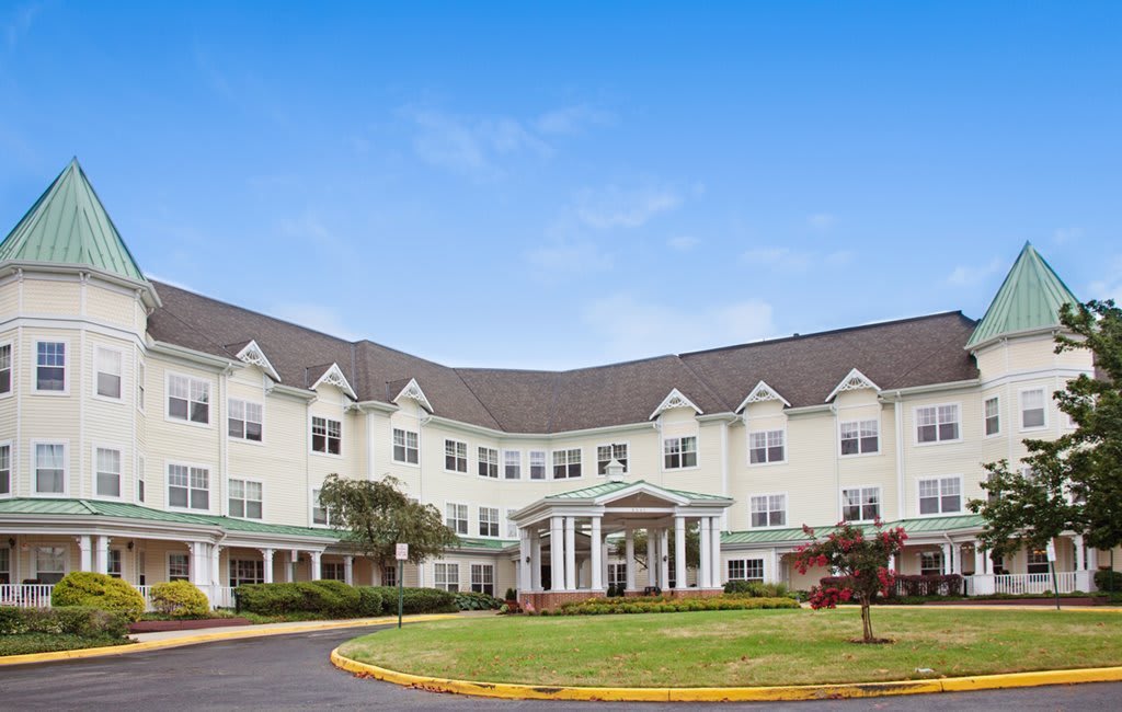 A large, white residential building with multiple windows and a landscaped front yard.
