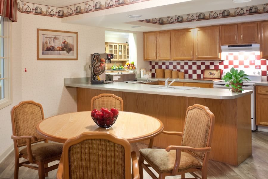 A cozy kitchen and dining area with a round table and chairs, featuring wooden cabinets and a checkered backsplash.