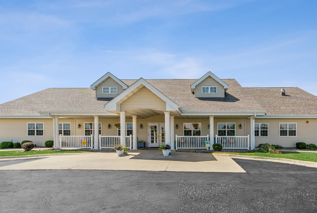 A large residential building with a gabled roof and a front porch area, captured during the daytime.