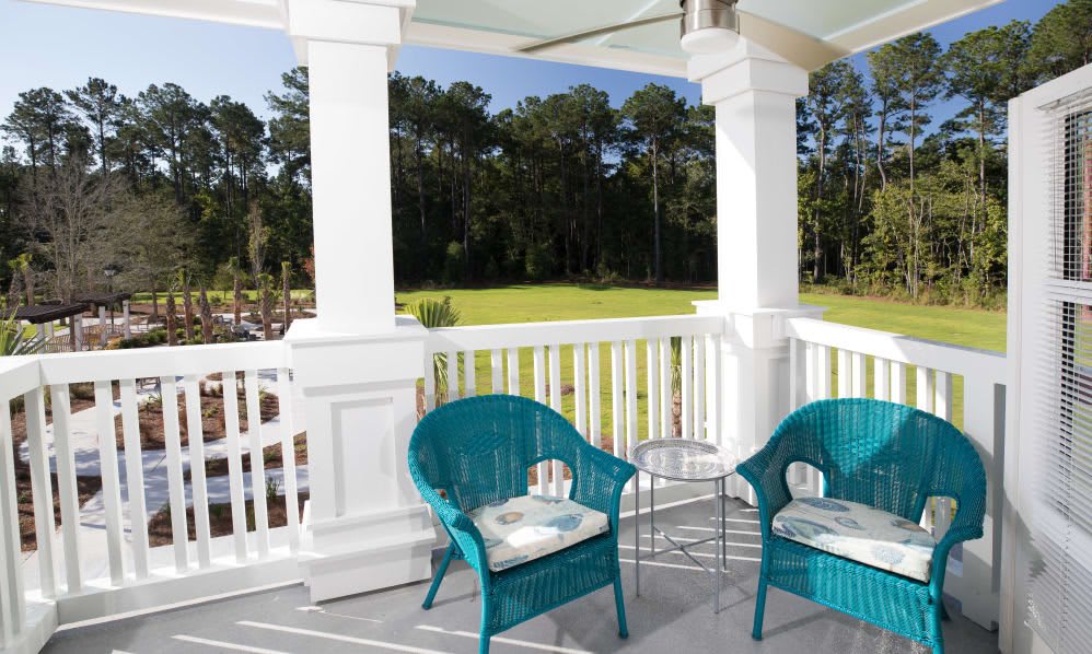 A serene balcony with teal wicker chairs and a small table, overlooking a lush green landscape.