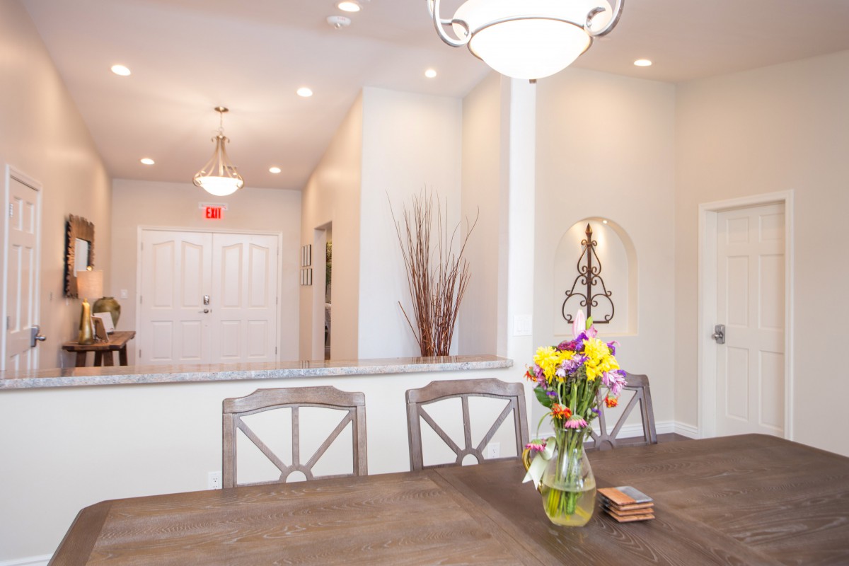 A modern dining room with a wooden table, chairs, and a vase of flowers under elegant lighting.