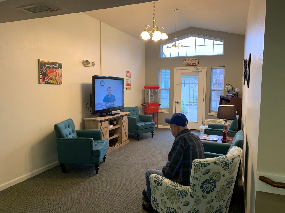 A cozy living room with a person watching television, surrounded by comfortable seating and warm lighting.