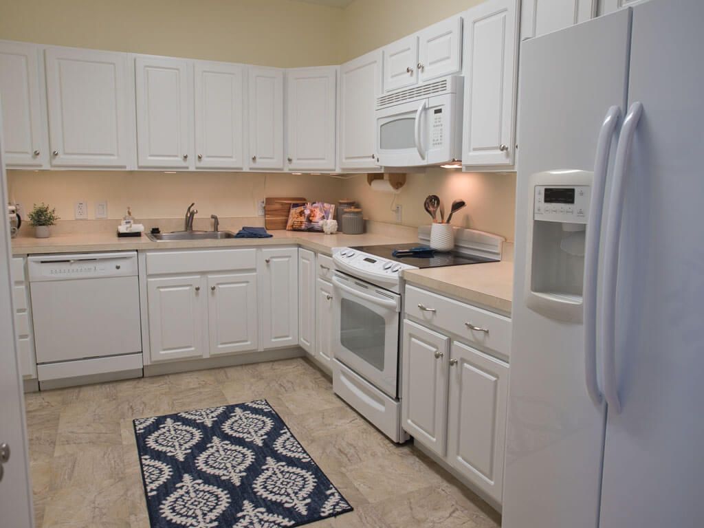 A modern kitchen with white cabinets and appliances, featuring a decorative rug on the tile floor.