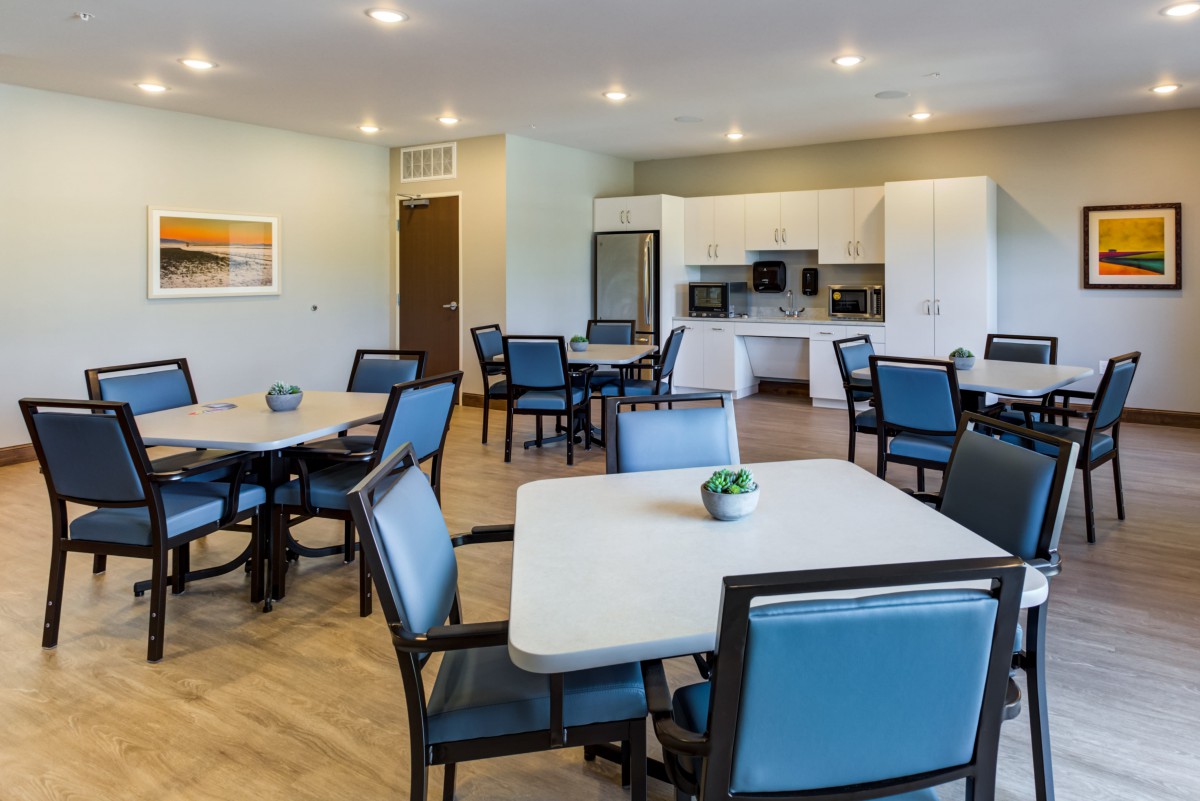 A modern dining area with tables and chairs, adjacent to a kitchen.