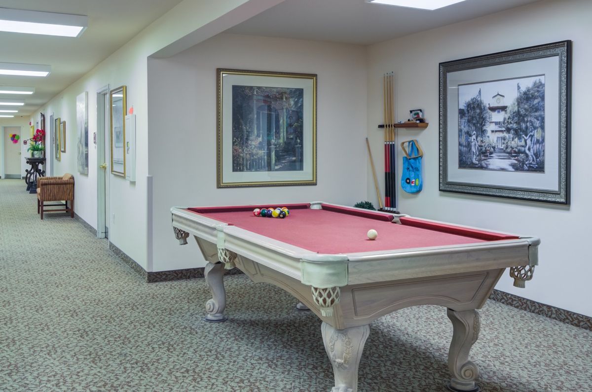 A game room with a red felt pool table, wall art, and cue sticks on a holder.