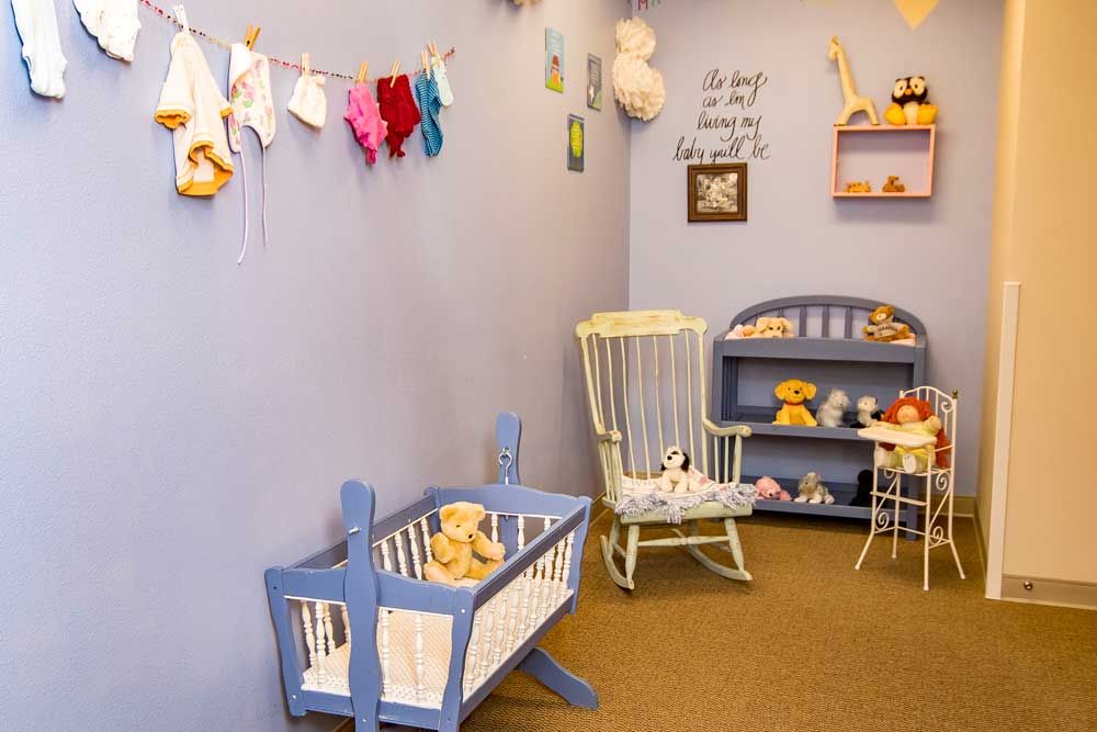 A cozy nursery room with a blue crib, rocking chair, and shelves filled with stuffed animals and toys.
