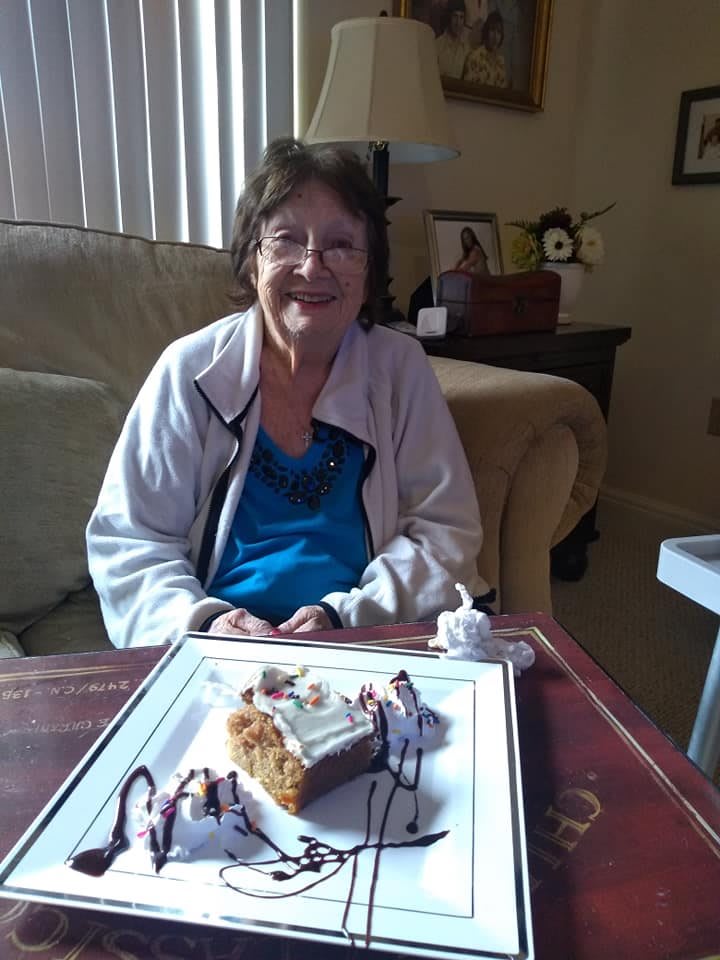 A smiling person sits in front of a decorated cake, ready to celebrate indoors.