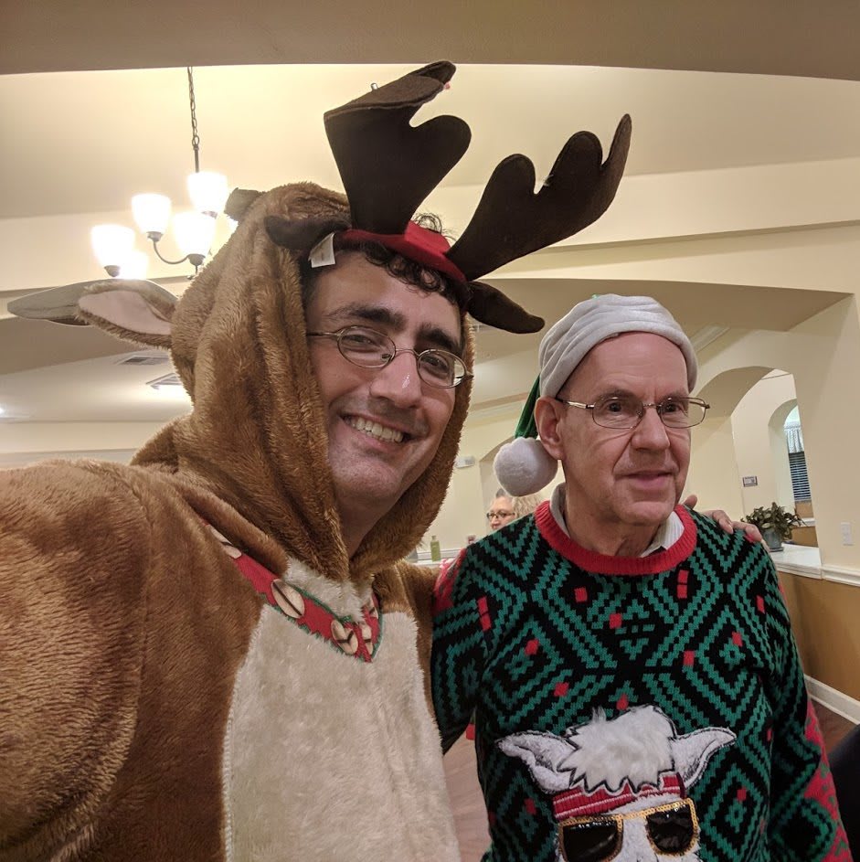 Two people dressed in festive holiday attire, one in a reindeer costume and the other wearing a Christmas sweater.