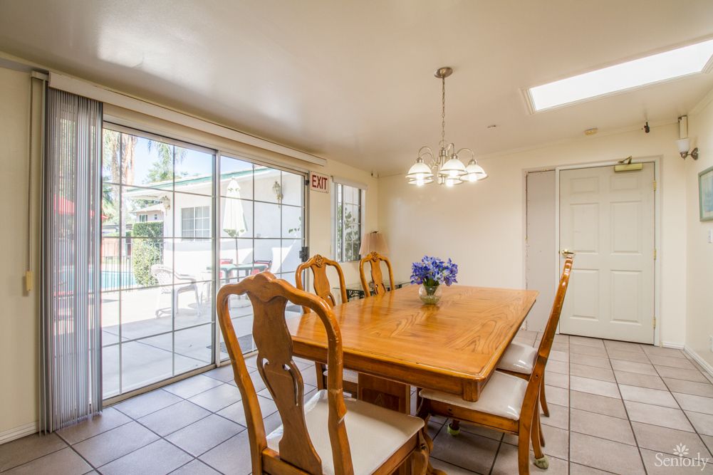 A bright dining room with a wooden table and chairs, illuminated by a chandelier and natural light from sliding glass doors.