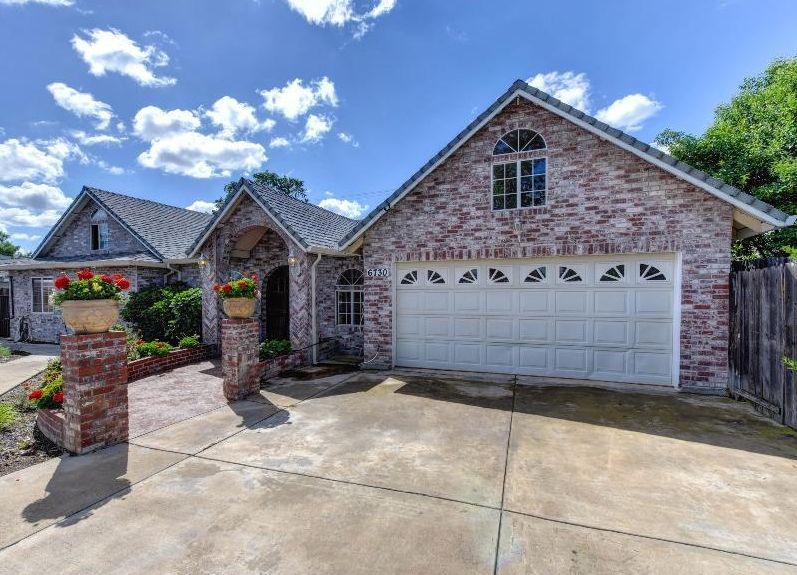 A suburban brick house with a garage and driveway under a blue sky.