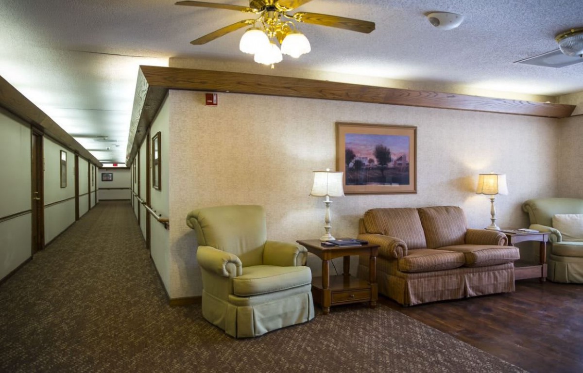 A cozy living room with a couch, armchair, lamp, and ceiling fan.