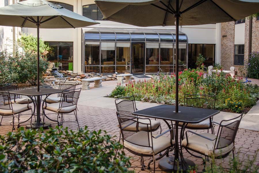 Outdoor patio with tables and chairs under umbrellas, surrounded by a garden.
