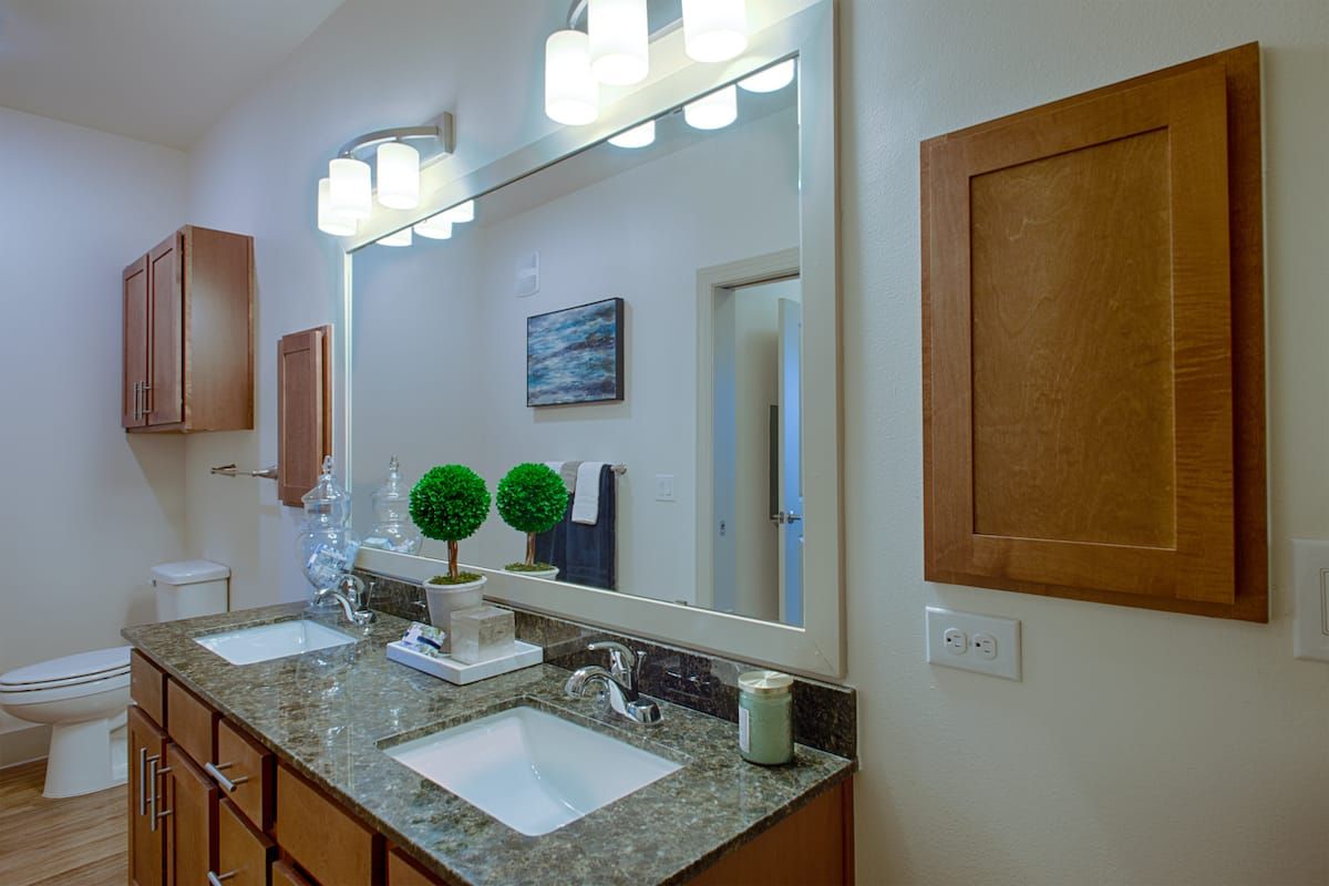 A modern bathroom featuring a large mirror, dual sinks with granite countertops, and elegant lighting.