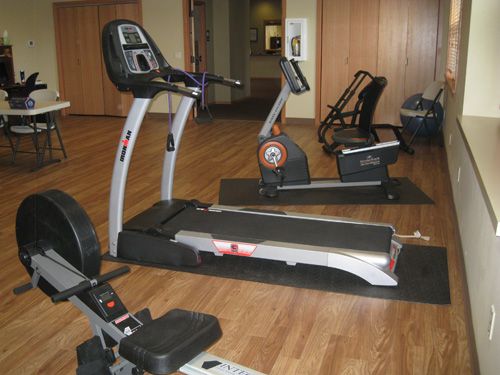 A gym room with various exercise equipment including a treadmill and stationary bikes.