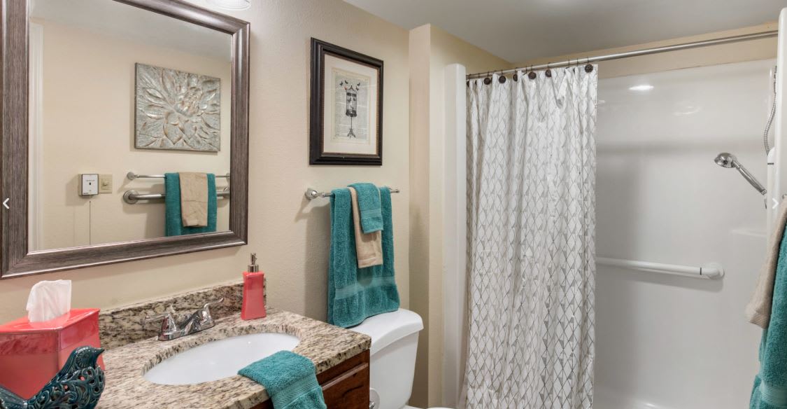 A neatly organized bathroom with a granite countertop, turquoise towels, and a patterned shower curtain.