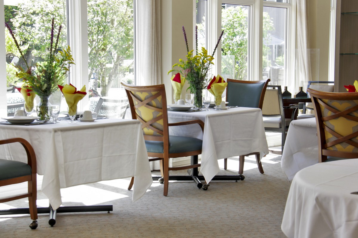 A bright and elegant dining area with tables set with white tablecloths and floral centerpieces.
