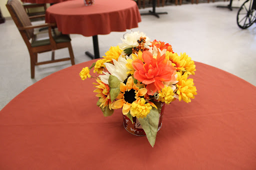 A vibrant floral arrangement featuring orange and yellow flowers in a vase, placed on a table with a red tablecloth.