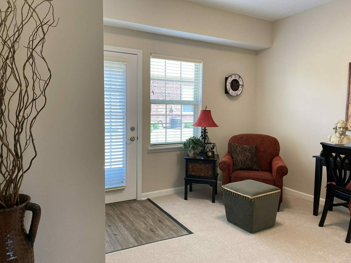 A cozy corner in a living room with an armchair, lamp, potted plant, and a window next to a door.