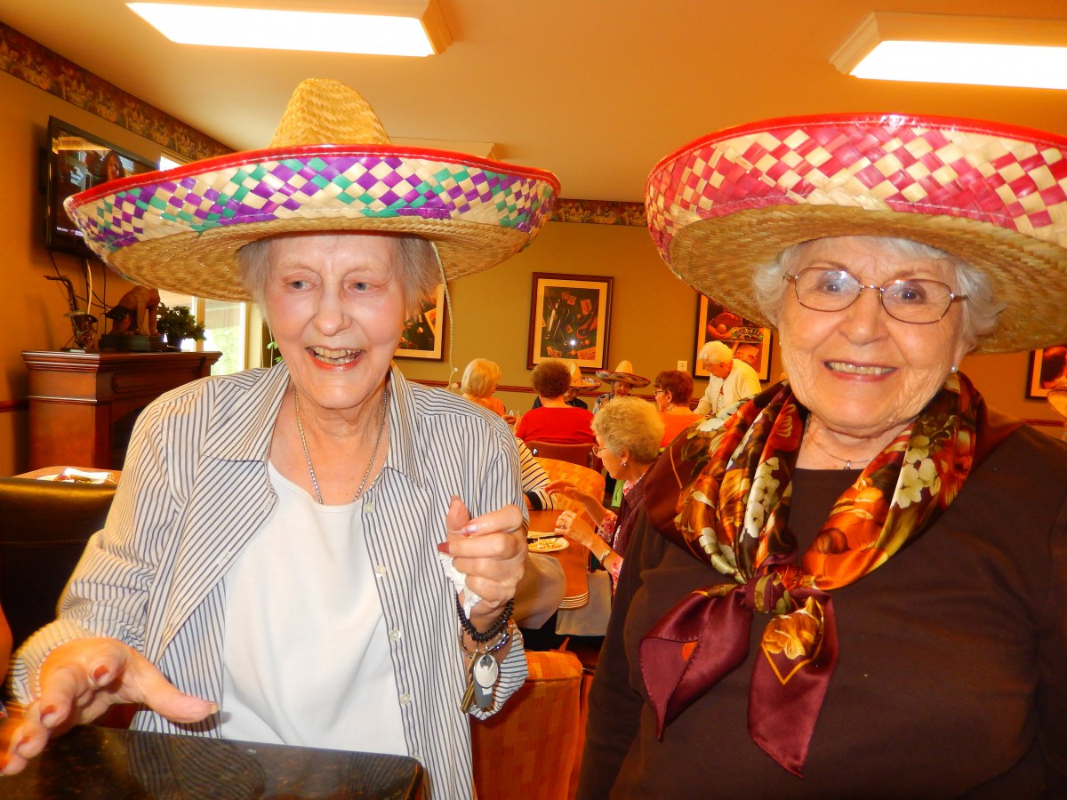 Two elderly women enjoy a celebration, wearing colorful sombreros and smiling brightly.