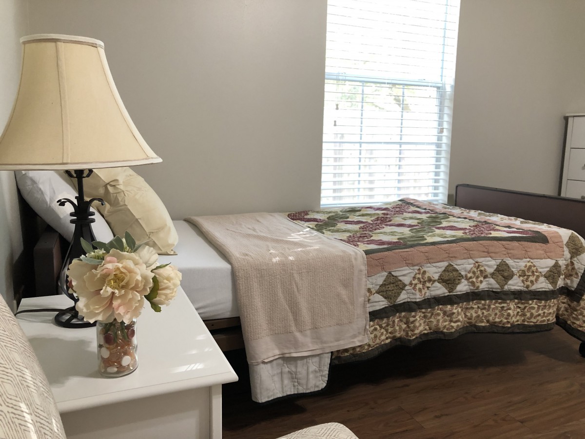 A cozy bedroom with a quilt-covered bed, a bedside lamp, and a vase of flowers.