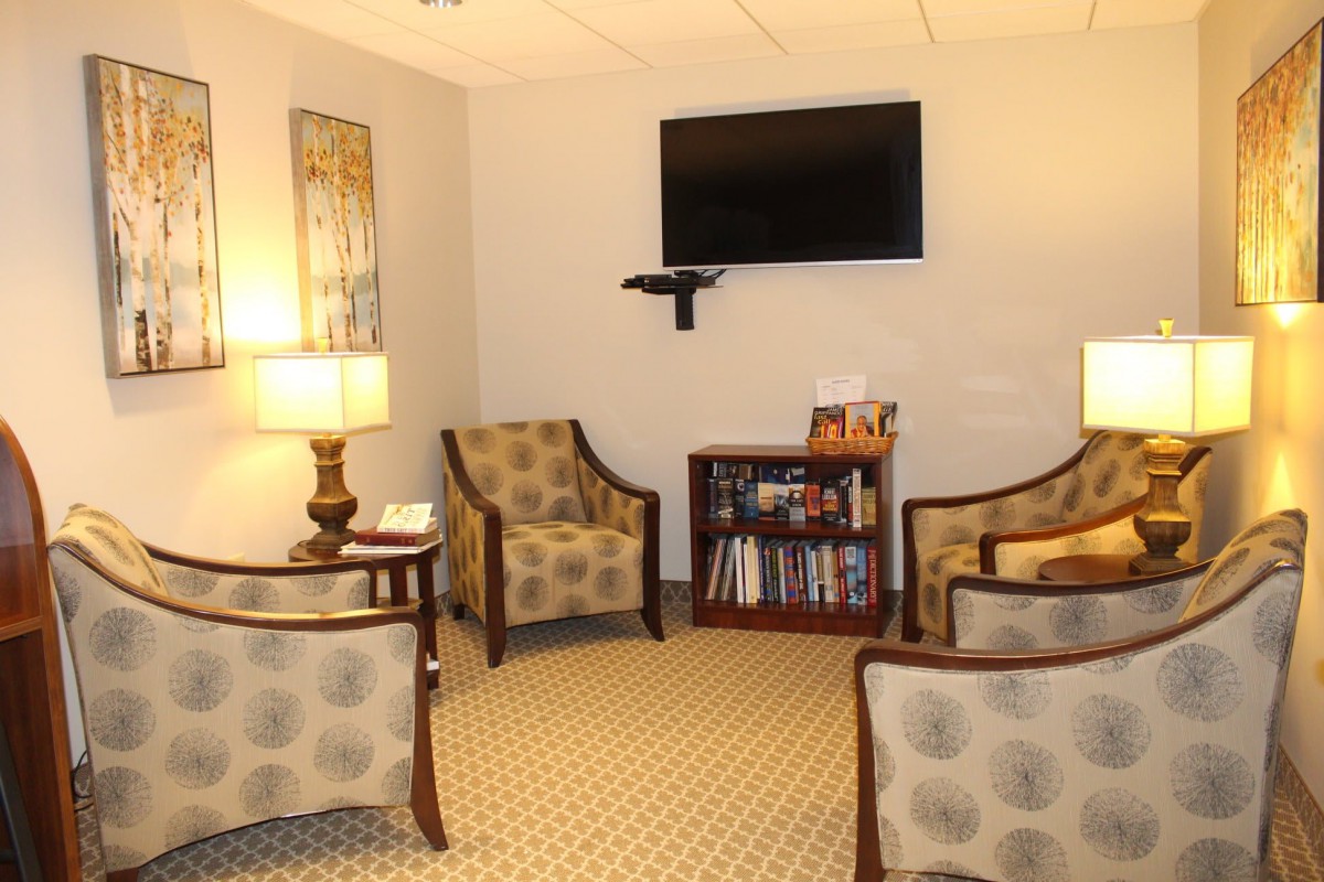 A cozy waiting room with comfortable chairs, a television, and a bookshelf.