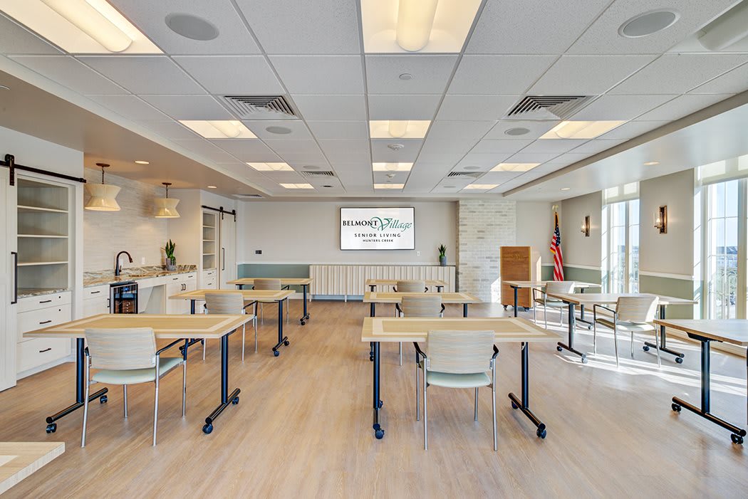 A modern conference room with tables and chairs arranged in rows facing a presentation screen.